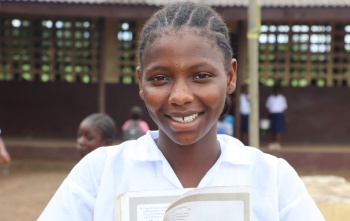 Isatu, a girl from Liberia, smiling outside her school