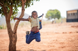 Boy jumps in celebration by a tree in Zambia