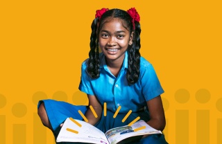 Girl smiling at camera with open book in lap against yellow background