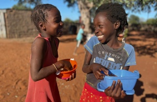 Happy children in Mozambique outside eating Mary's Meals