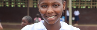 Isatu, a girl from Liberia, smiling outside her school