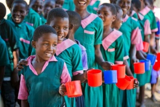 Children queuing and smiling holding red and blue cups