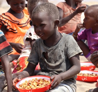 Ng’asike, a pre-school boy, sitting eating a bowl of maize and beans amongst other children