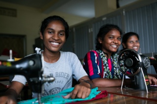 three girls smiling and using sewing machine