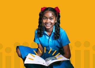 Girl smiling at camera with open book in lap against yellow background