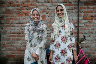 Two young women, Fatima and Soni, stand outside, laughing