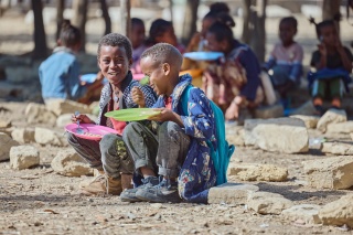 Two boys laugh with each other while sitting outside eating Mary's Meals in Ethiopia