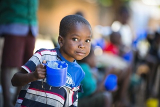 A small boy in Malawi carrying a mug of Mary's Meals porridge