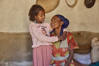 A mother and daughter embrace in their home