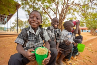 Children in Zambia sit outside with mugs of mugs of Mary's Meals porridge