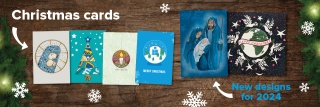 A selection of Christmas cards sit on a festive wooden background with snowflakes and Christmas tree branches