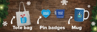 Mary's Meals tote mug, pin badges and mug sits on a festive wooden background with snowflakes and Christmas tree branches