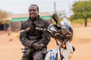 Amos Lungu, a school feeding officer from Zambia, sits on a motorbike