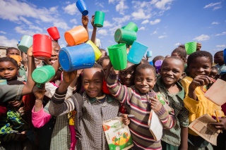 A big group of happy children outside in Zambia holding mugs up in the air